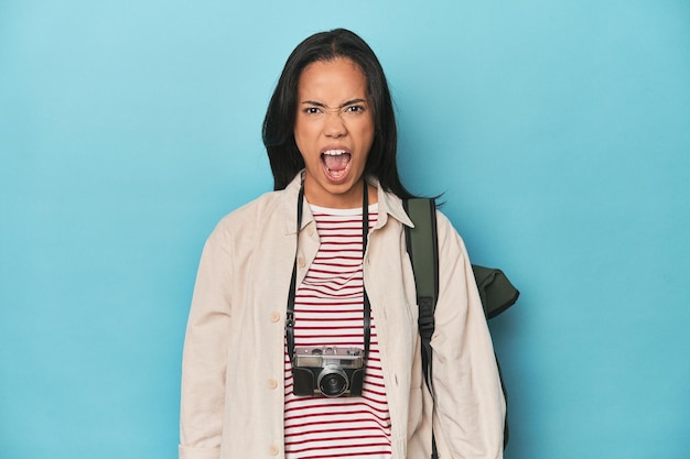 Filipina woman with camera and backpack on blue screaming very angry and aggressive