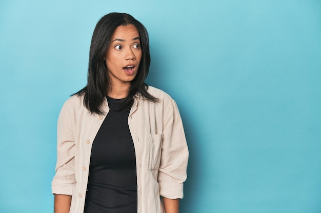 Filipina young woman on blue studio being shocked because of something she has seen