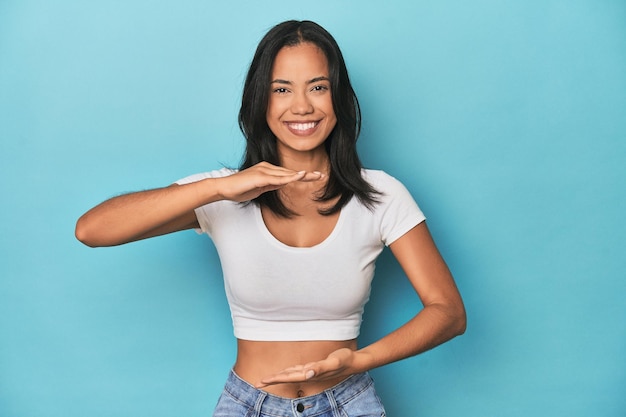 Filipina young woman on blue studio holding something with both hands product presentation