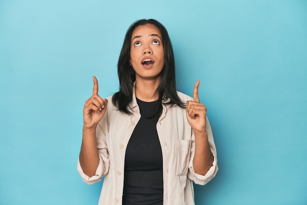 Filipina young woman on blue studio pointing upside with opened mouth