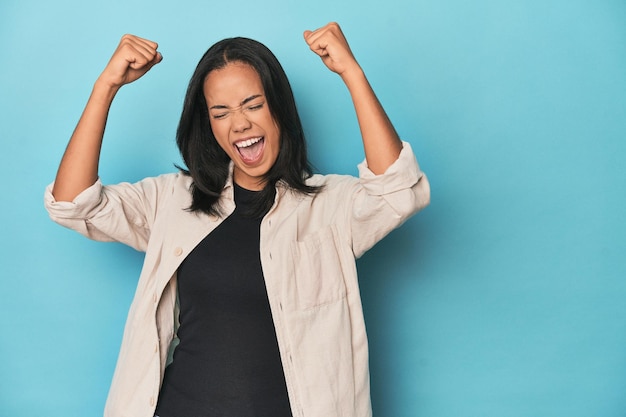 Filipina young woman on blue studio raising fist after a victory winner concept