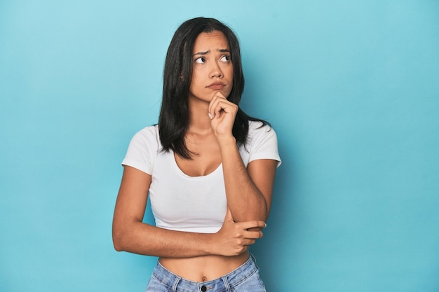 Filipina young woman on blue studio thinking and looking up being reflective contemplating