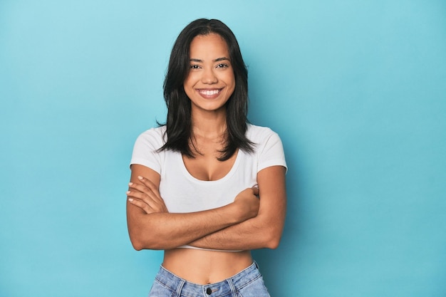 Filipina young woman on blue studio who feels confident crossing arms with determination