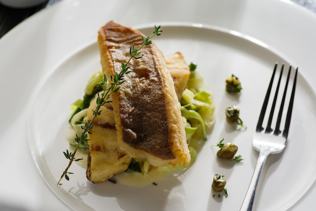 Photo fillet of halibut on a pillow of stewed leeks on the white plate.