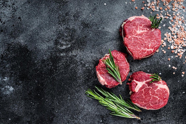 Fillet Mignon tenderloin raw meat beef steaks on butchery table. Black background. Top view. Copy space.