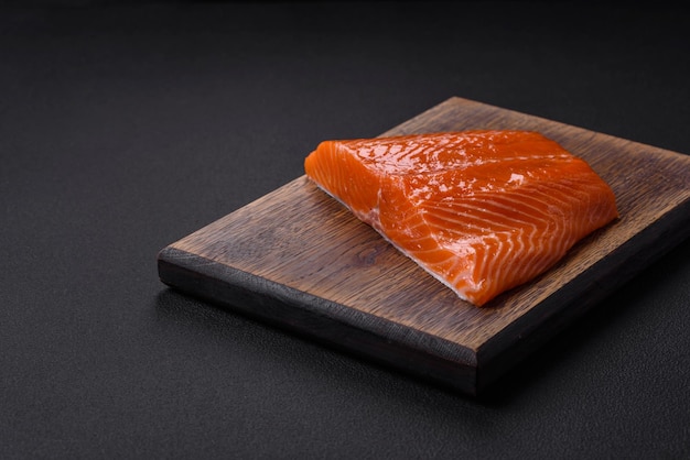 Photo fillet of raw red salmon fish with salt spices and herbs on a dark concrete background