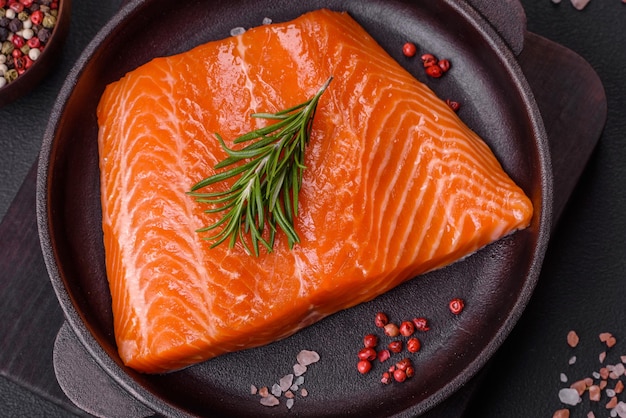 Fillet of raw red salmon fish with salt spices and herbs on a dark concrete background