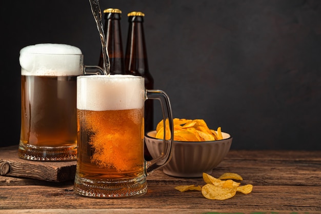 Filling beer mugs with beer on the background of chips and bottles Oktoberfest