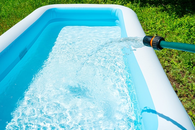 Filling the inflatable pool with water. Swimming pool in the summer garden. Side view, horizontal.