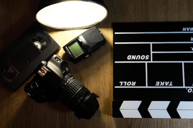 Film clapper with a camera, a microphone and a VHS tape on wood.