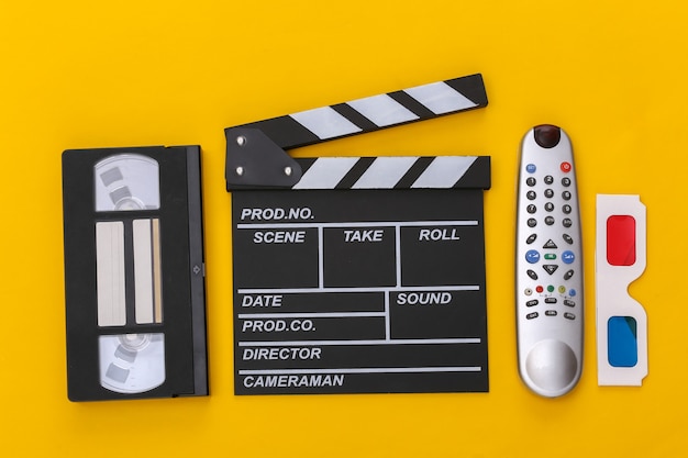 Film klepel bord, 3D-bril, videocassette en tv-afstandsbediening op gele achtergrond. Bovenaanzicht