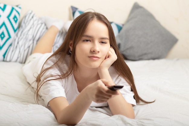 Film e novità di serie la ragazza è sdraiata a casa sul letto con un telecomando in mano a guardare la tv