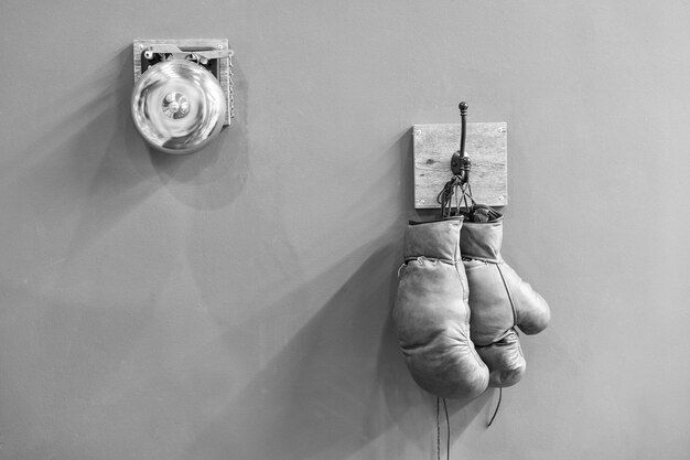 Final sparring Vintage boxing gloves hang on hook wall background Boxing gloves and ring bell Boxing career famous sportsman Museum of box sport Box exhibition retro attributes Boxing school