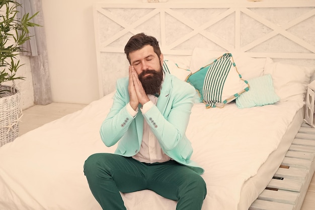 Finalmente in camera da letto un'altra lunga giornata è finita sentirsi stanco e assonnato ragazzo assonnato in abiti formali uomo seduto sul letto gesto del sonno mancanza di sonno bisogno di più sonno orario serale uomo d'affari esausto