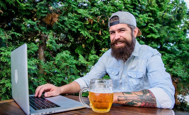 Finally friday Brutal man leisure with beer and online game Hipster relax sit terrace outdoors with beer Bearded hipster freelancer enjoy end of working day with beer mug He deserve this pint