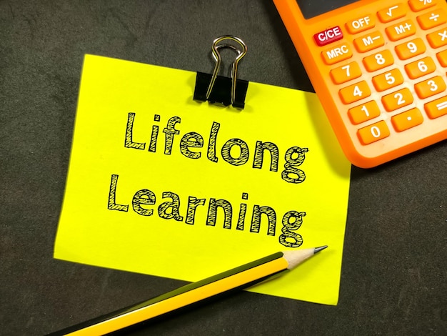 Foto finance concepttext levenslang leren op kleurrijke papieren notitie met rekenmachine en potlood op zwarte achtergrond
