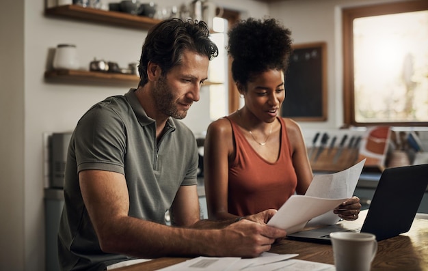 finance couple and laptop in a kitchen for planning budget and savings or paying bills together in their home marriage online and people with documents for tax mortgage or home loan or insurance