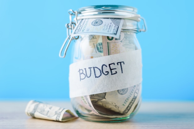 Finance and investment concept. Glass saving bank with dollar bills and inscription budget on a blue background