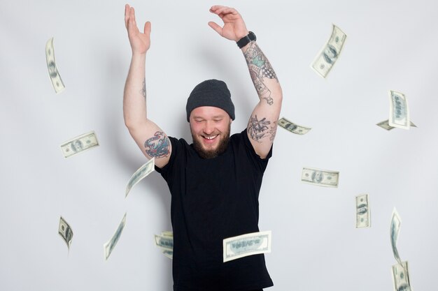 Finance, people, lifestyle concept - Young man with money to camera. Dollars. fashion Portrait young bearded man. Smiling Hipster boy.handsome man hat. Brutal bearded boy with tattoo