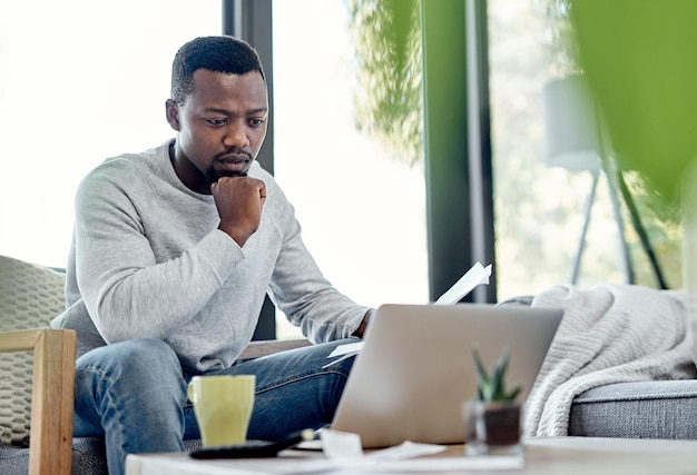 Finance stress and worried black man paying bills on a laptop while doing paperwork at home Concerned anxious male checking budget getting bad news or negative feedback of a rejected loan or debt