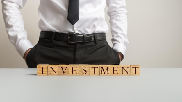 Financial business adviser standing behind a desk with an Investment sign made of wooden blocks on it.