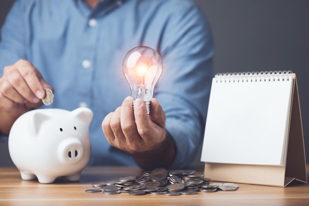 Foto calcolo e pianificazione finanziaria piano annuale intelligente per risparmiare denaro uomo con lampadina con pila di monete salvadanaio e calendario da tavolo 2023 sul tavolo studio girato su sfondo scuro