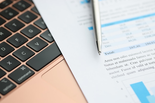 財務書類とペンはノートパソコンのキーボードにあります。ビジネスレポートオンラインコンセプト