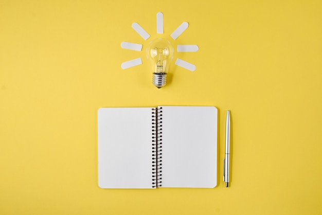 Financial planning table top with pen, notepad, light bulb on yellow background. 