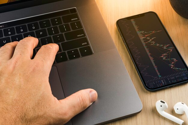 Financial stock market graph on the smartphone screen on wooden background with a computer beside it. Stock Exchange.