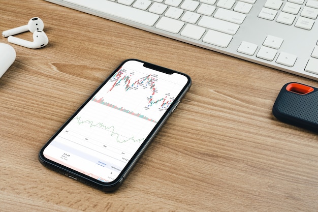 Financial stock market graph on the smartphone screen on wooden background with a computer beside it. Top view. Stock Exchange.