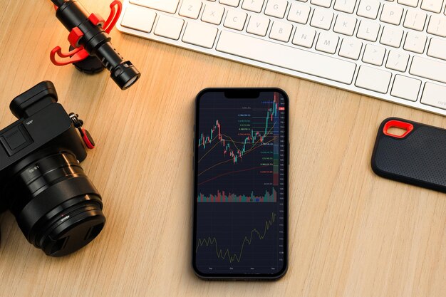 Financiële beursgrafiek op het smartphonescherm. content creator-omgeving met toetsenbord, camera en microfoon. beurs.