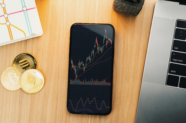 Financiële beursgrafiek op smartphonescherm op houten tafel met cryptocurrencies-munten en computer Kantooromgeving Stock Exchange