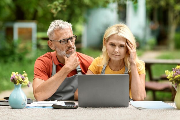 Foto financiële crisis verstoord senior paar met behulp van laptop zittend aan tafel in de tuin