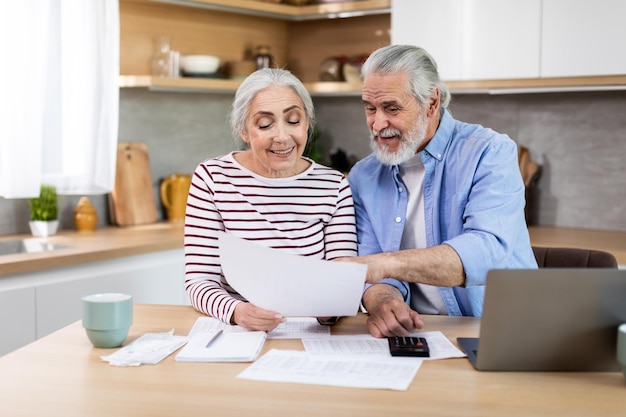 Financiële planning op pensioen Senior koppel met laptop en papieren in de keuken