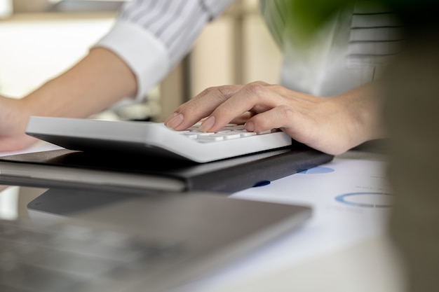 Financiële zakenvrouw die op een witte rekenmachine drukt, gebruikt een rekenmachine om de cijfers te berekenen in de financiële documenten van het bedrijf die medewerkers op de afdeling maken als vergaderdocumenten.