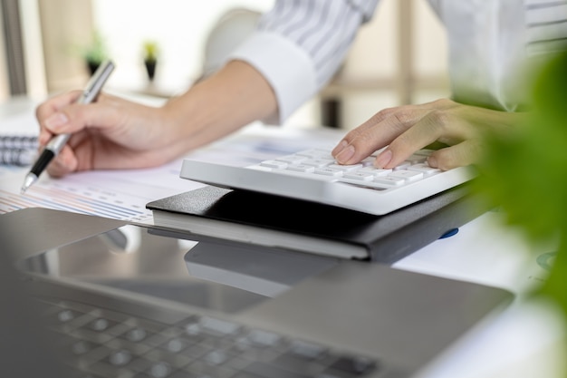 Financiële zakenvrouw die op een witte rekenmachine drukt, gebruikt een rekenmachine om de cijfers te berekenen in de financiële documenten van het bedrijf die medewerkers op de afdeling maken als vergaderdocumenten.