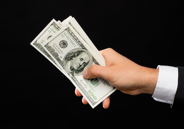 financiën, mensen, besparingen en rijkdom concept - close-up van mannelijke handen met dollar contant geld op zwarte achtergrond