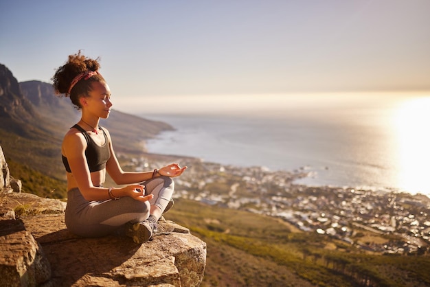 Find yourself and be that Shot of a young woman meditating while sitting on a mountain cliff