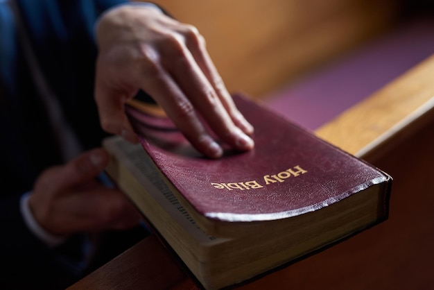 Находя утешение в хорошей книге Обрезанный снимок мужчины, открывающего Библию, сидящего на скамье в церкви