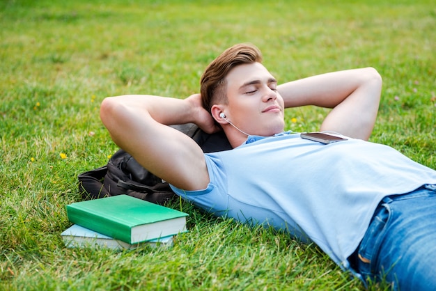 Finding a peaceful place to relax. Handsome young man holding hands behind head and smiling while lying on grass and listening to MP3 Player