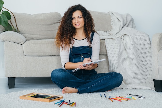 fine art hobby. female artist sitting relaxed on floor with paint color swatch and pencils