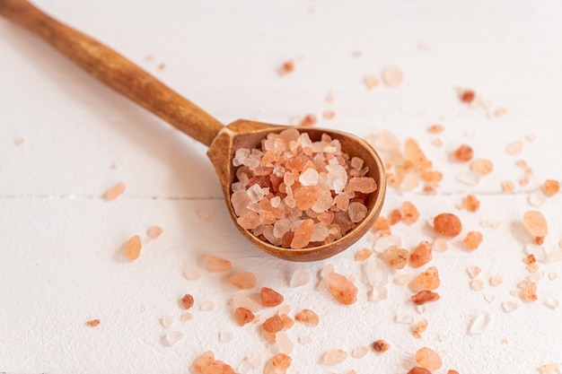 Fine himalayan salt in a wooden scoop on a white background.