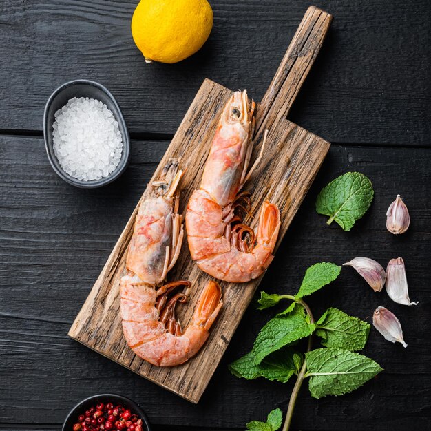 Fine selection of tiger shrimps on wooden board on black wooden table, top view, food photo.