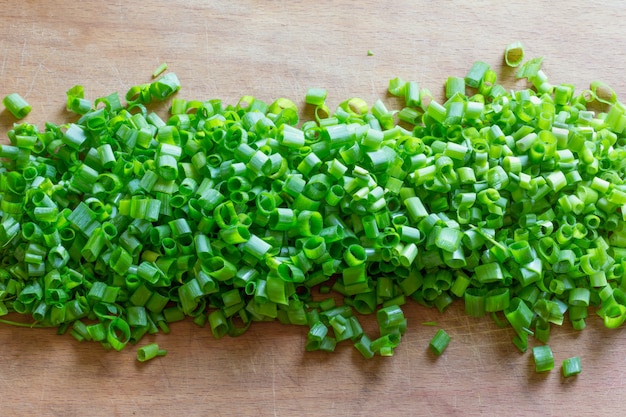 Finely chopped green onions in the middle of an old wooden cutting board close-up view from above