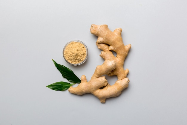 Finely dry Ginger powder in bowl with green leaves isolated on colored background top view flat lay
