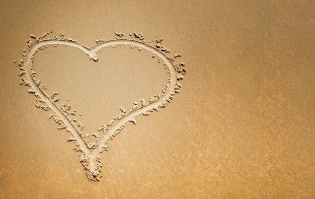 Photo finger drawn heart on the sand symbol of love with copy space