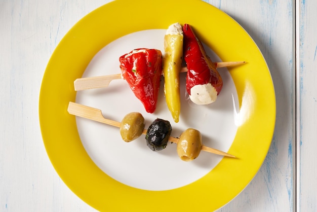 Finger food sticks with olives and stuffed pepperoni on yellow plate.