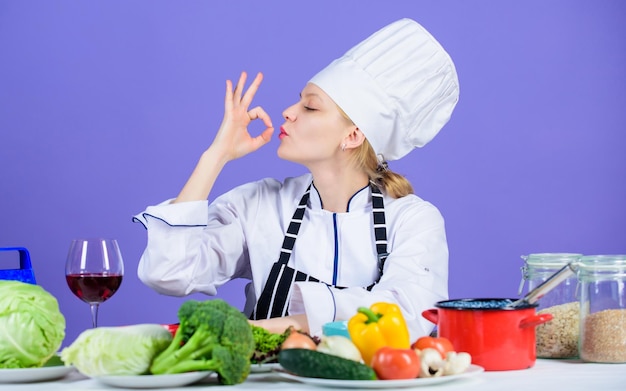 Photo finger licking good pretty woman chef gesturing ok kitchen maid preparing vitamin food professional cook with vitamin vegetables on table vitamin nutrition getting vitamin the natural way