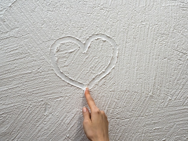 Finger paints a heart on a white stucco wall. Valentine's day concept.