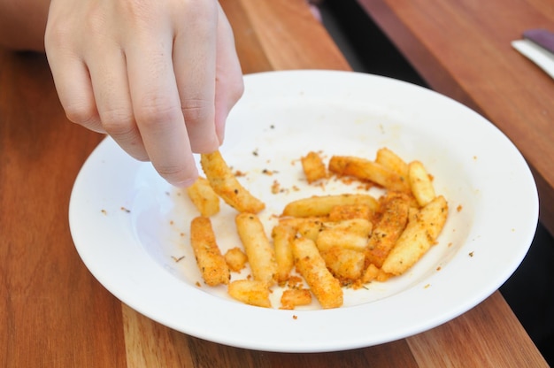 Finger picking golden french fries from a plate